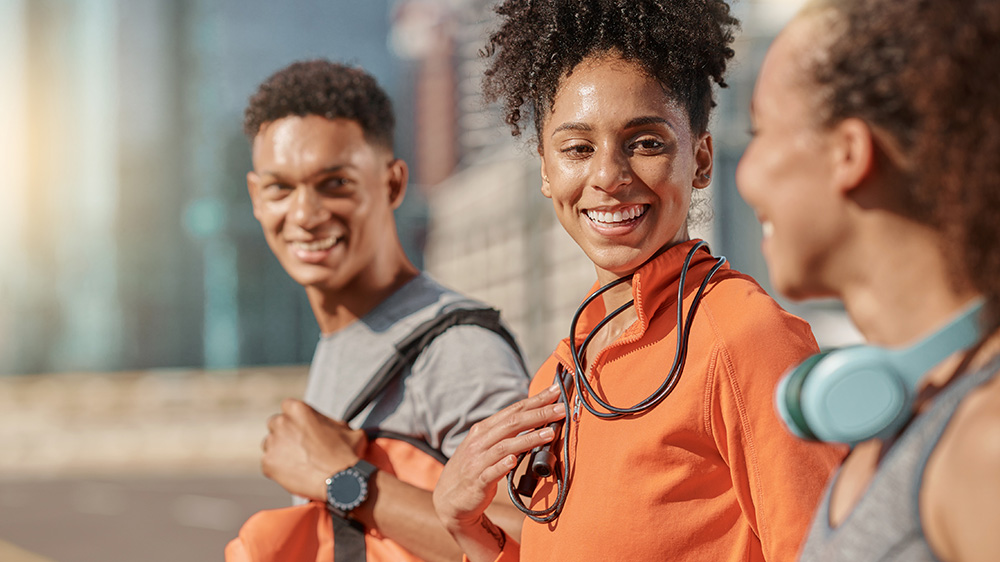Three adults smiling in the outdoors off to do a fitness activity